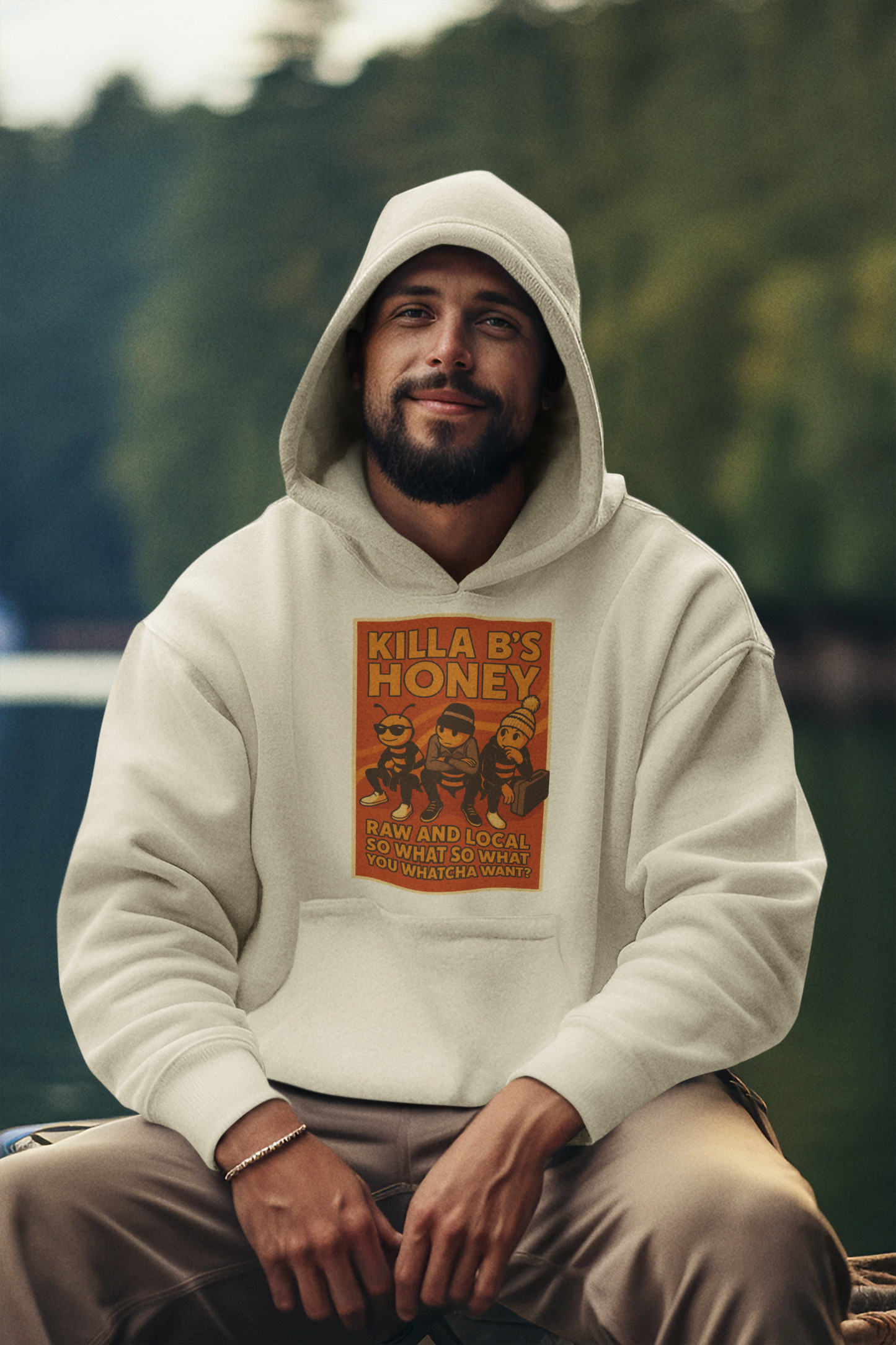 Man smiling knowing he's wearing the coolest honey streetwear brand, a Beastie Boys themed "Killa B's Honey" hoodie with a graphic design sitting outdoors.