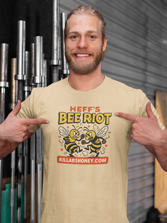 Man wearing a beige t-shirt with a bee riot themed graphic and text, pointing at the shirt.