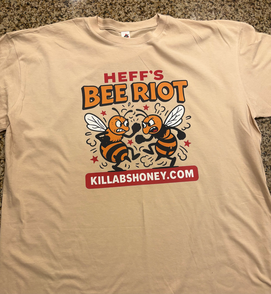 Beige t-shirt with 'Heff's Bee Riot' graphic and website text on a textured surface