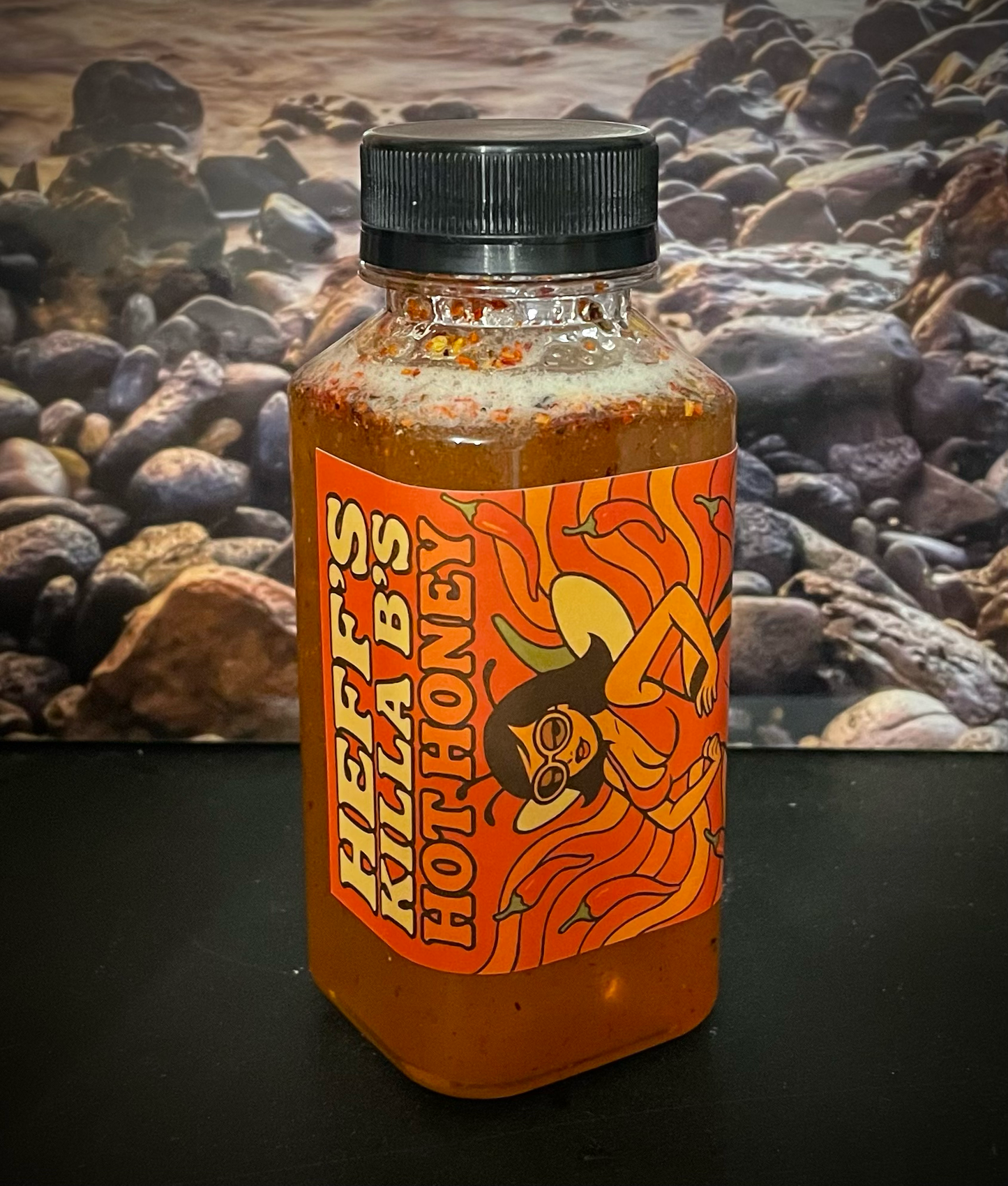 Bottle of Heff's Killa Bees Hot Honey with a colorful label against a rocky background