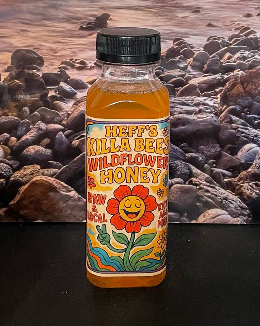 Bottle of Heff's Killa Bees Wildflower Honey with a colorful label against a rocky background.