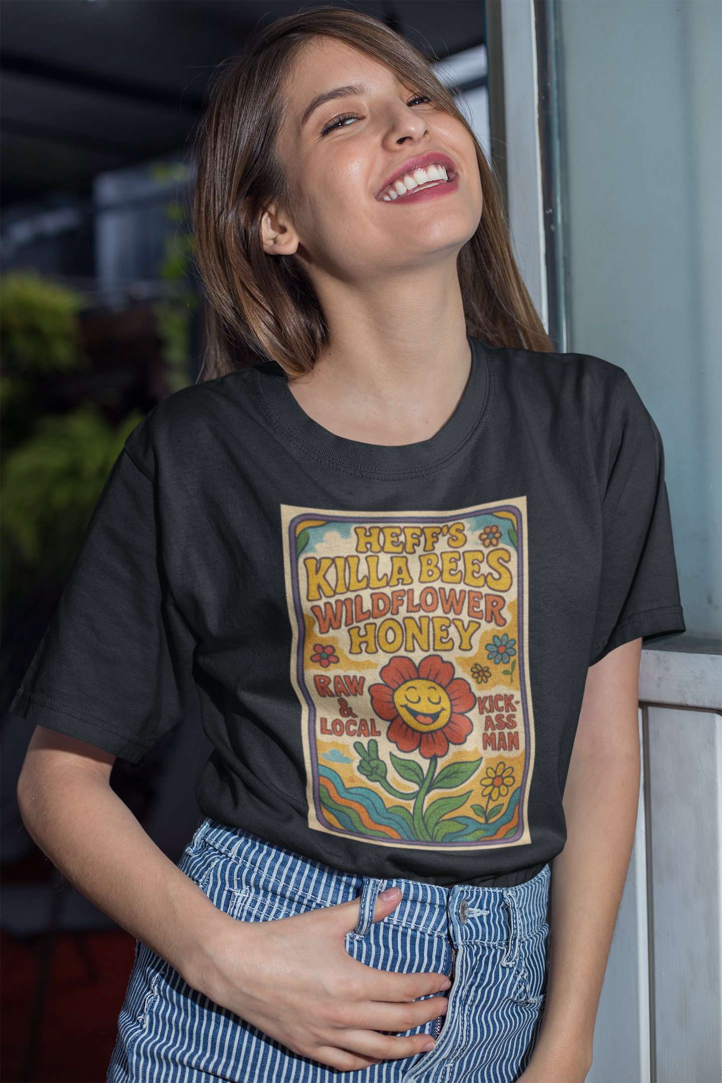 Woman wearing a black t-shirt with a colorful Heff's Killa Bees Wildflower Honey graphic design, standing indoors.