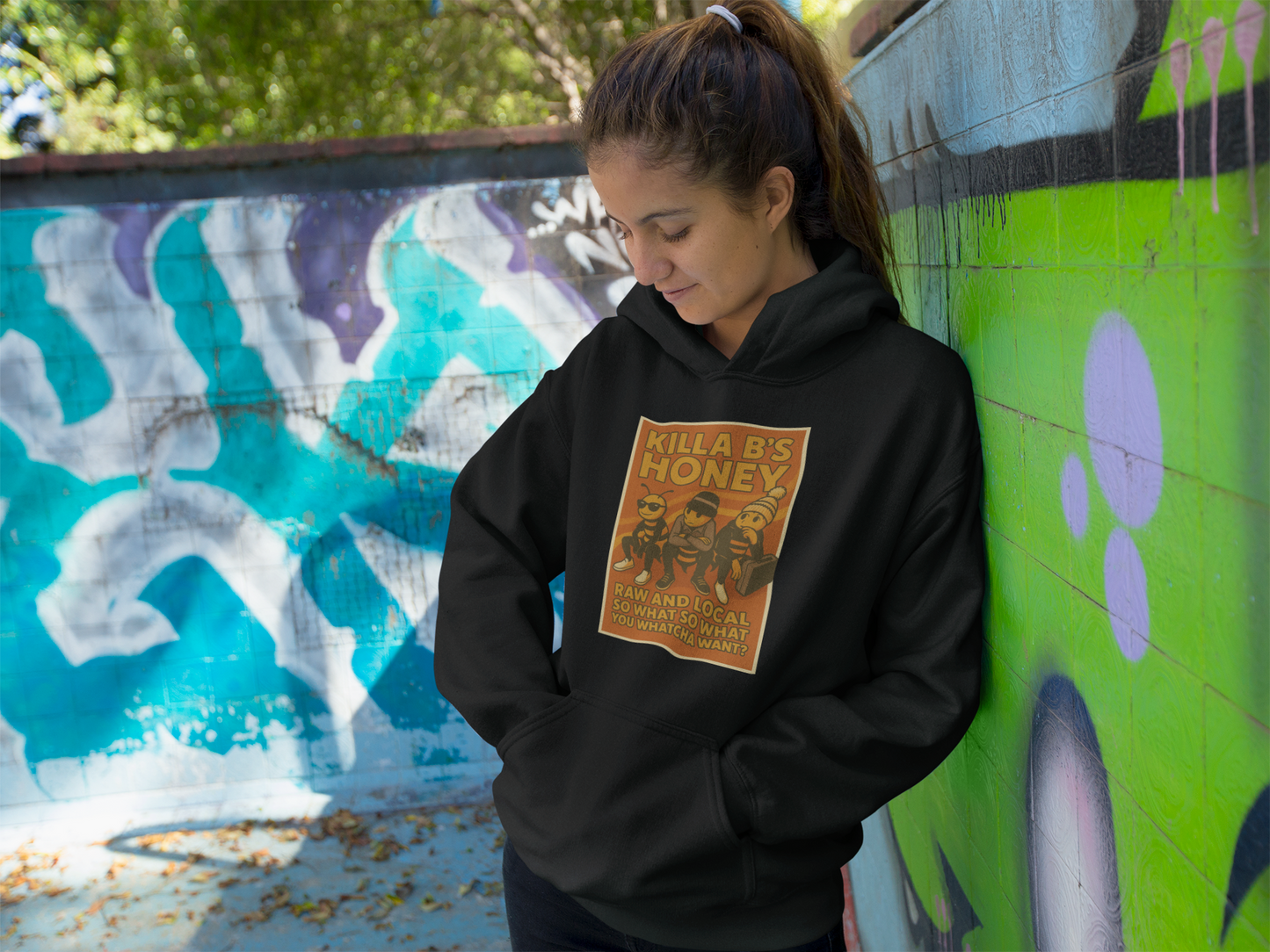 Person wearing a black hoodie with the Beastie Boys themed graphic design leaning against a graffiti-covered wall.